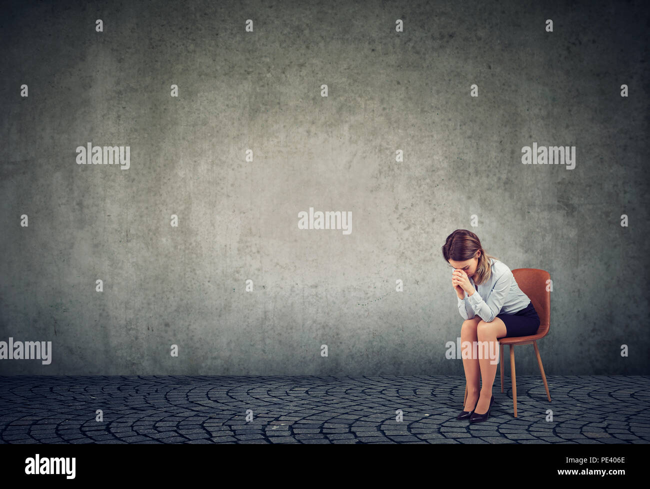 Jeune femme assise seule sur une chaise et se penchant sur les mains des problèmes et à la fatigue extrême sur fond gris Banque D'Images