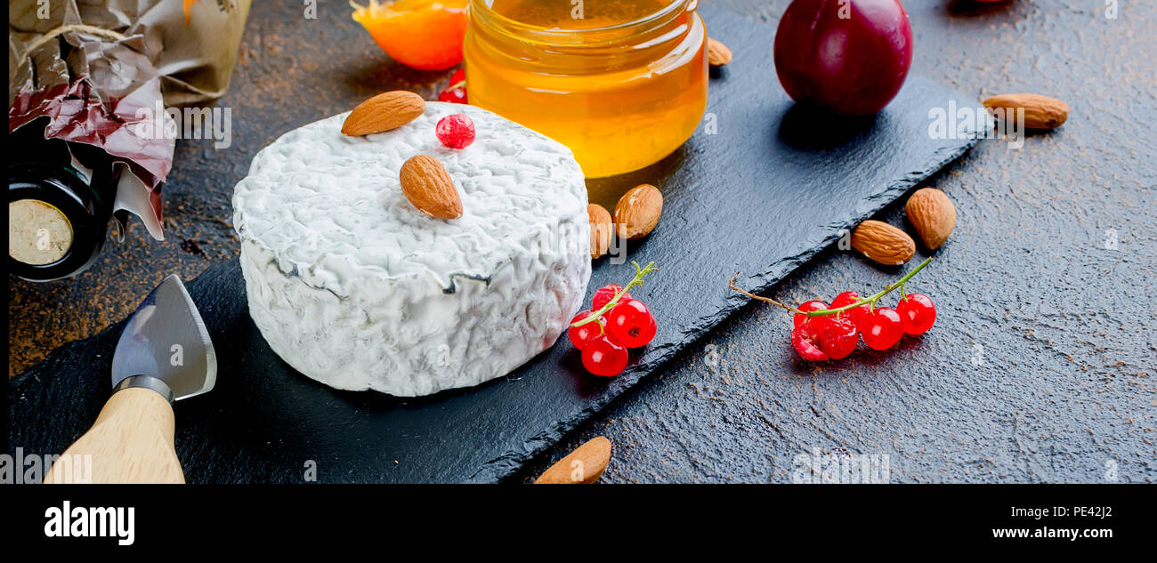 Tête ronde de fromage bleu avec du miel, de cassis, de fruits à coque et une bouteille de vin sur un tableau sombre, concept de gastronomie, fromage italien, romantique ev Banque D'Images