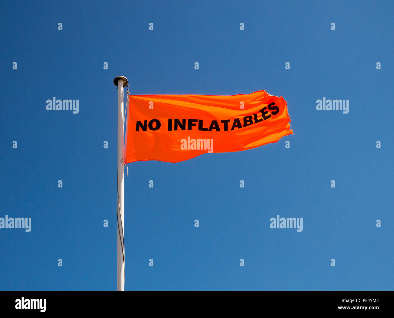 Image en couleur d'un drapeau orange avec pas de pneumatiques en lettres noires sur un mât métallique, tourné à partir de ci-dessous contre un ciel bleu clair Banque D'Images