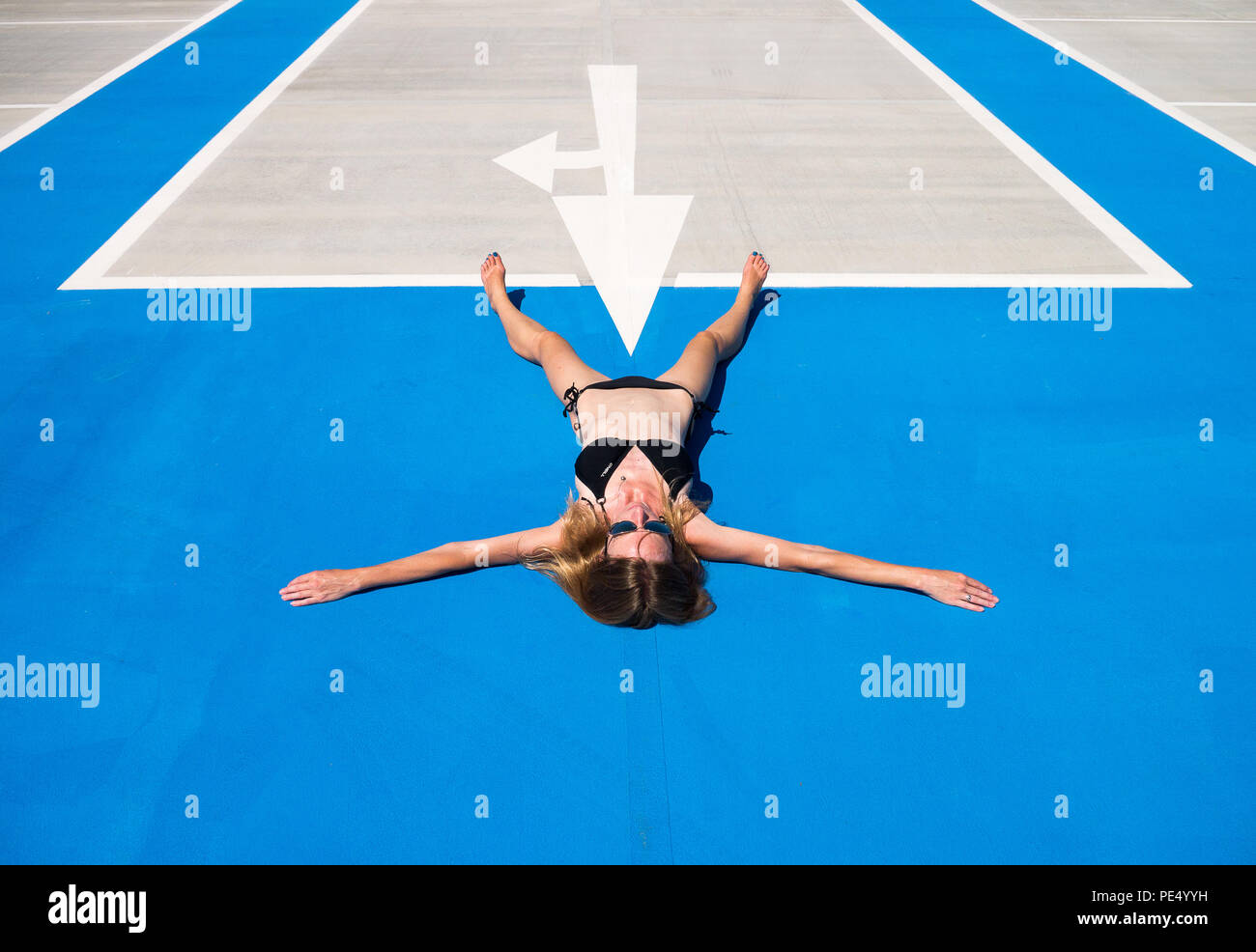 Image en couleur d'une femme blonde en bikini noir une spreadeagled couchée sur son dos sur l'asphalte, bleu avec une flèche blanche pointant vers entre ses jambes Banque D'Images