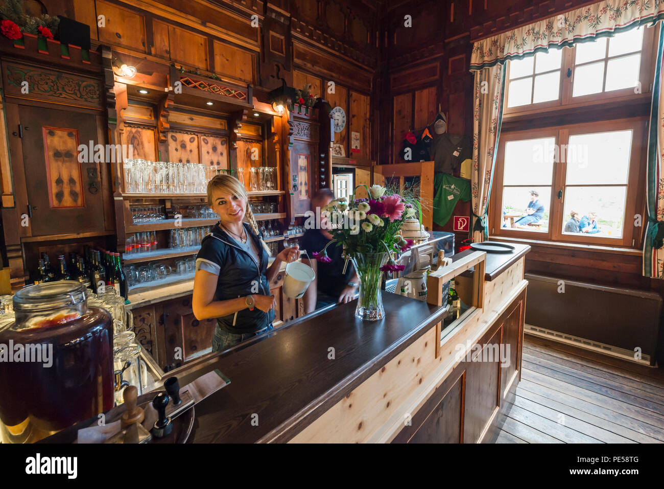 Femme blonde tresse avec derrière le comptoir du bar dans la magnifique salle à manger du refuge de montagne Berliner Hütte sourit à la caméra, Zillertal, Autriche Banque D'Images