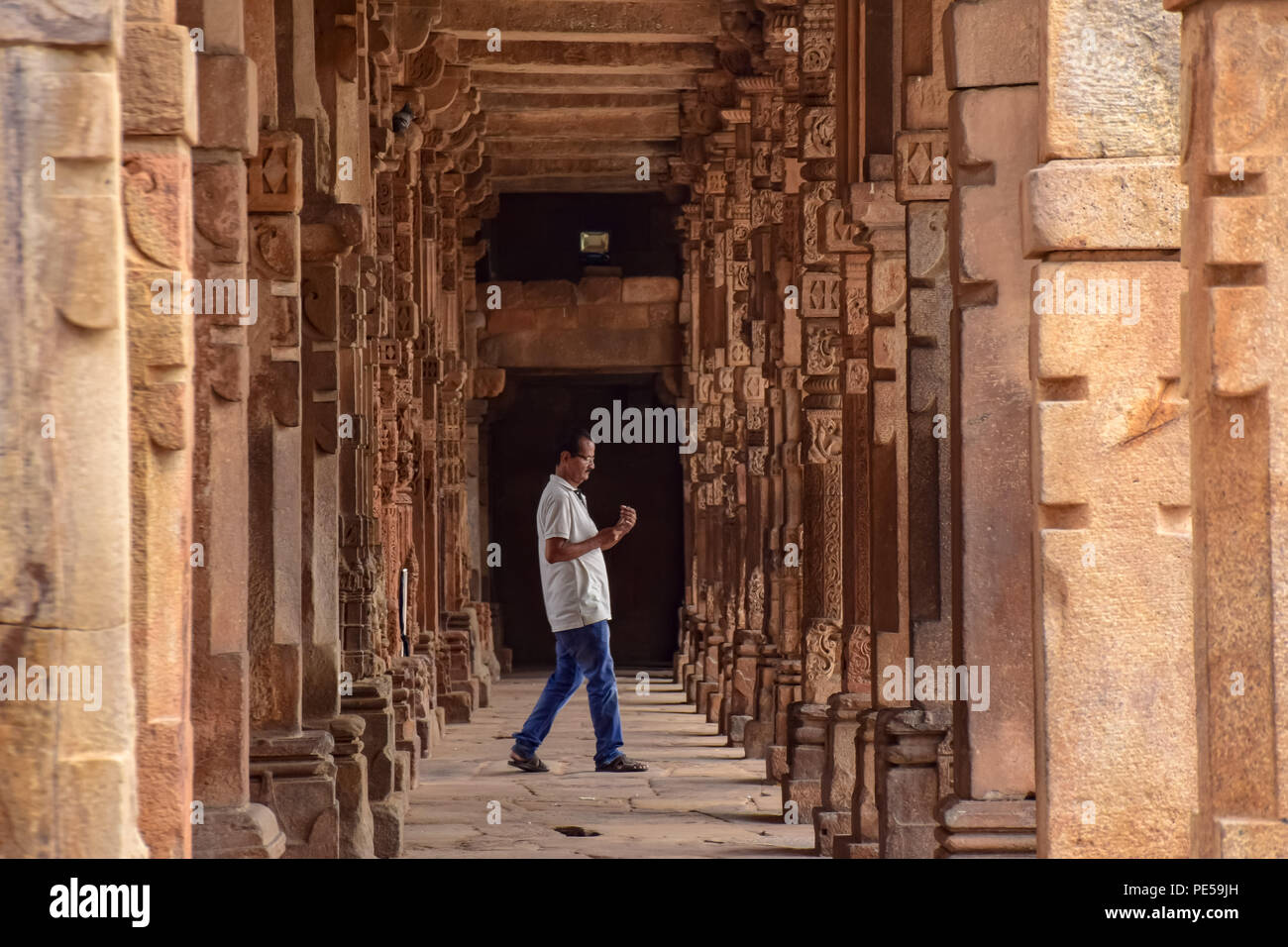 Un homme marche entre la série de colonnes à l'intérieur -Sculputed Quwwat ul -l'Islam mosquée de Qutub Complex à Delhi en Inde. Qûtb Minâr Comité permanent 73 mètres de haut à Delhi, est le plus haut minaret de briques et site du patrimoine de l'UNESCO. Il représente l'Indo -style architectural islamique, construit par Qutb-ud-Din Aibak comme une victoire Tower en 1192 A.D. Banque D'Images