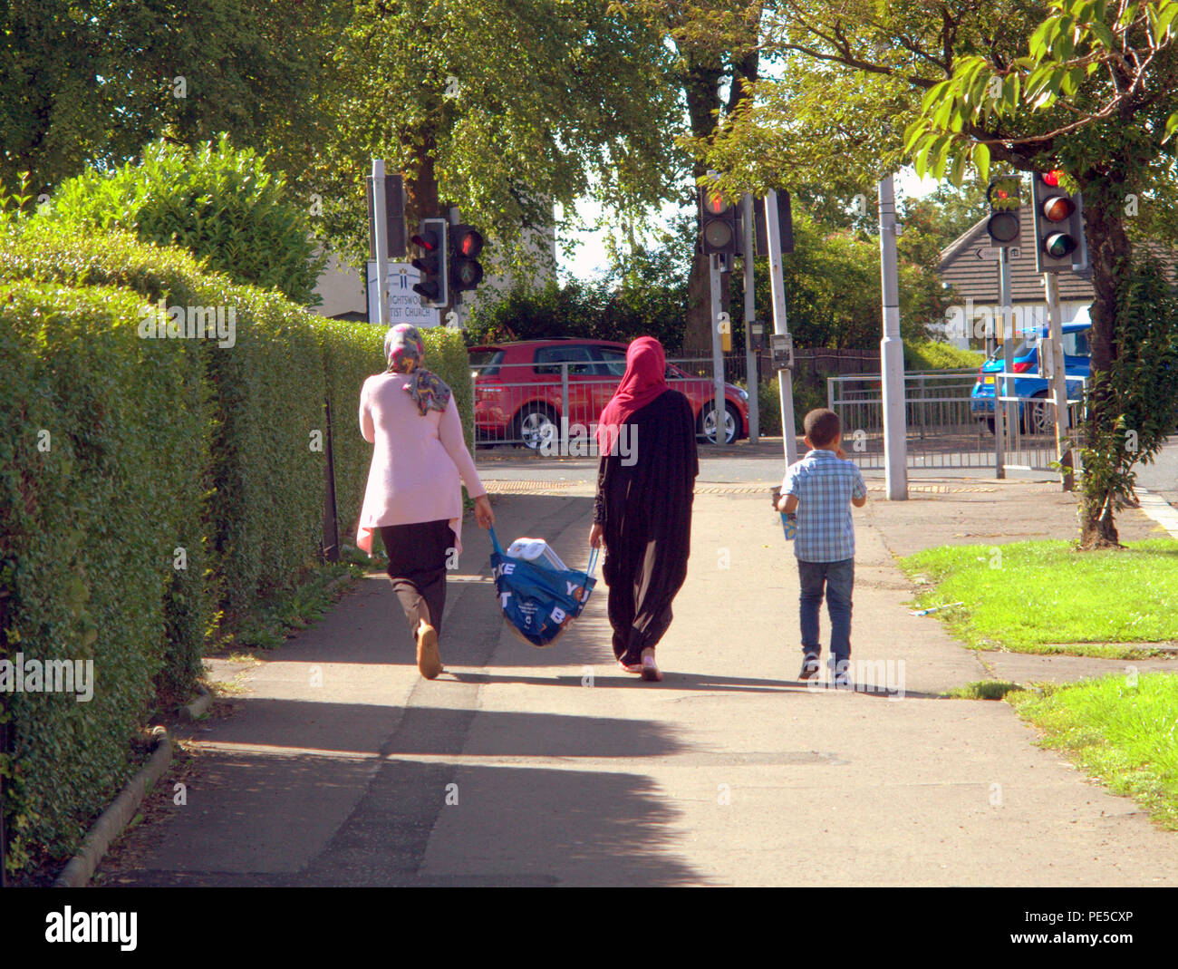 La famille musulmans musulmans panier hijab protège tête marcher sur la rue avec la famille enfant vu de derrière Glasgow, Royaume-Uni Banque D'Images