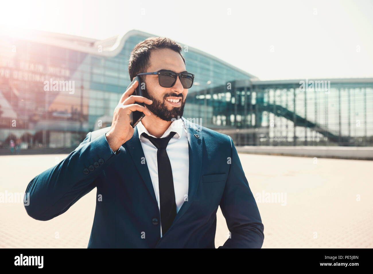 Smiling businessman barbu porte des lunettes de soleil et costume bleu  parler via smartphone avant bâtiment moderne élevé Photo Stock - Alamy