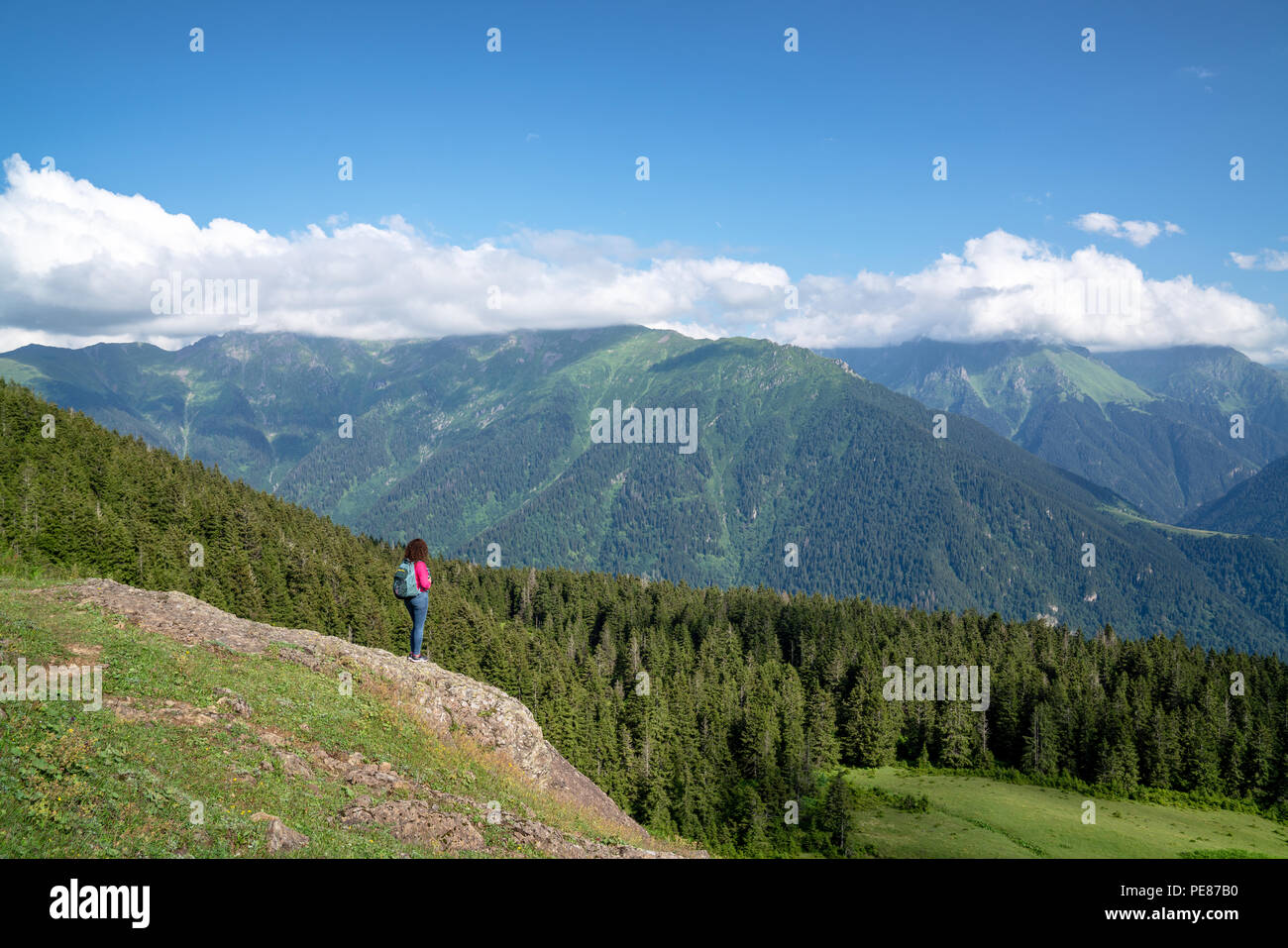 Jeune femme heureuse avec sac à dos, debout sur un rocher à la recherche d'une vallée au-dessous. Banque D'Images