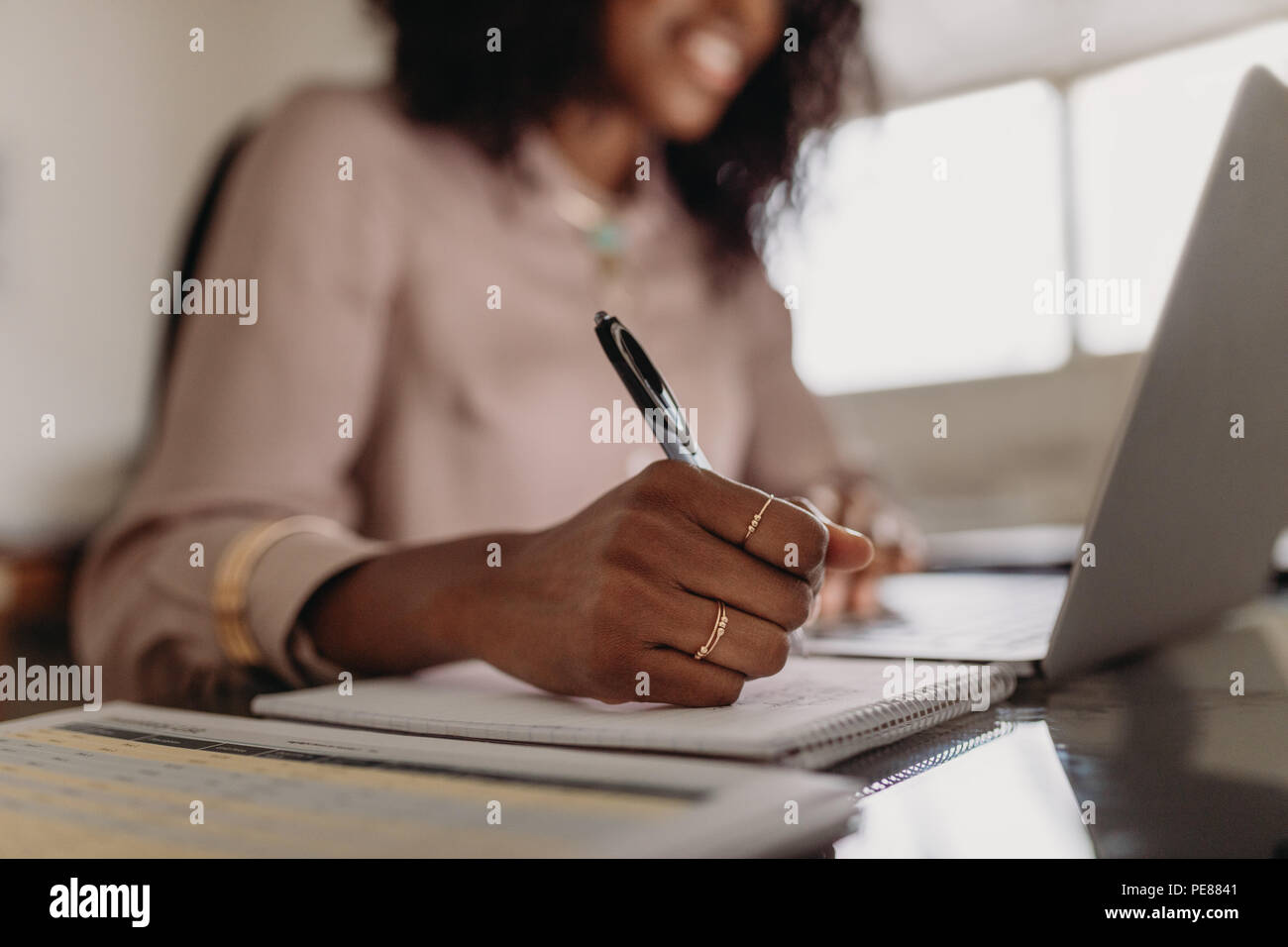 Businesswoman working on laptop computer assis à la maison. Close up de main d'une femme tenant un stylo et écrit sur le bloc-notes. Banque D'Images