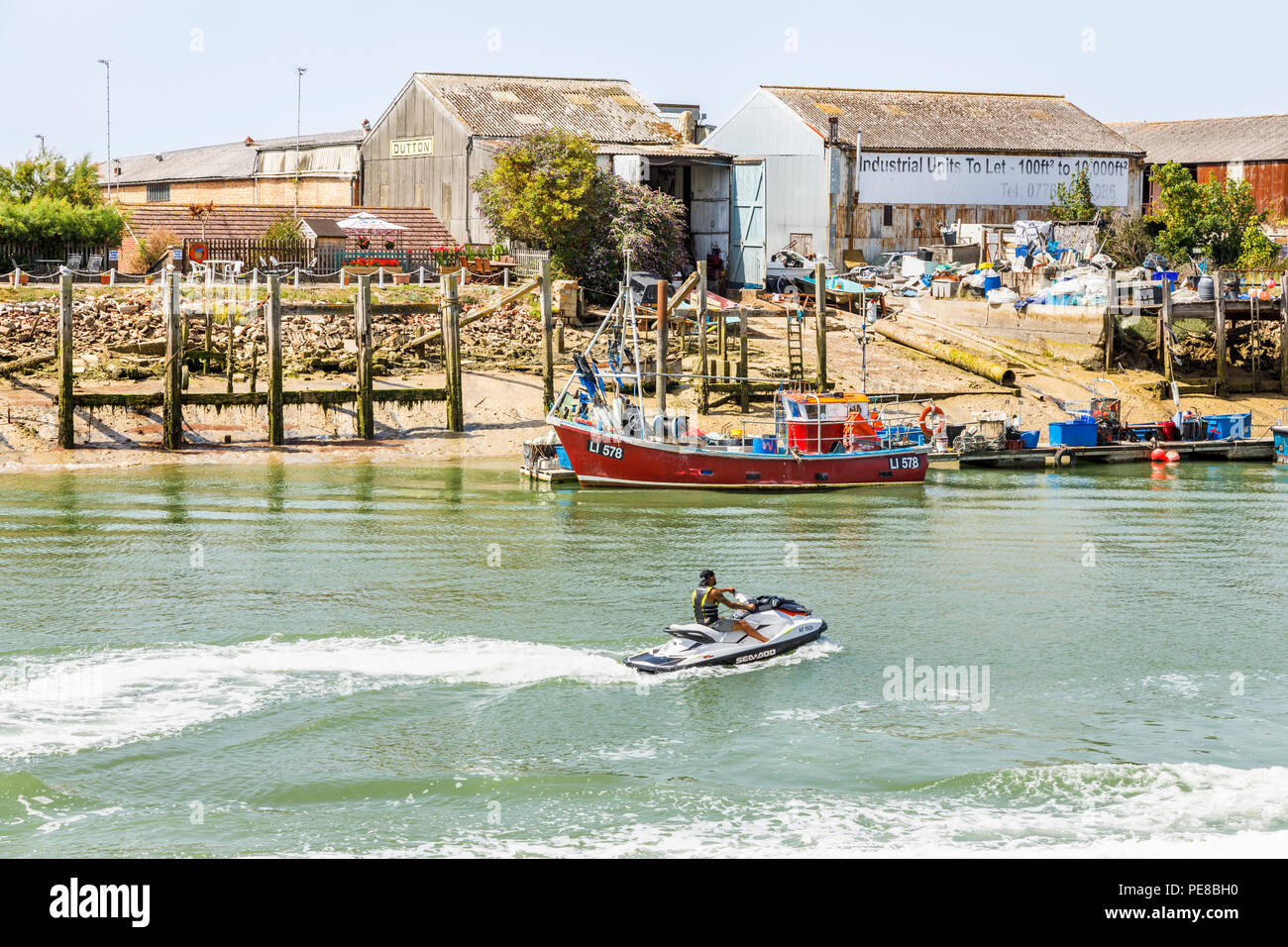 Par Jetski bateaux de pêche amarrés à des unités industrielles sur la rive sur la plage ouest de la rivière Arun estuaire, Littlehampton, West Sussex, UK Banque D'Images