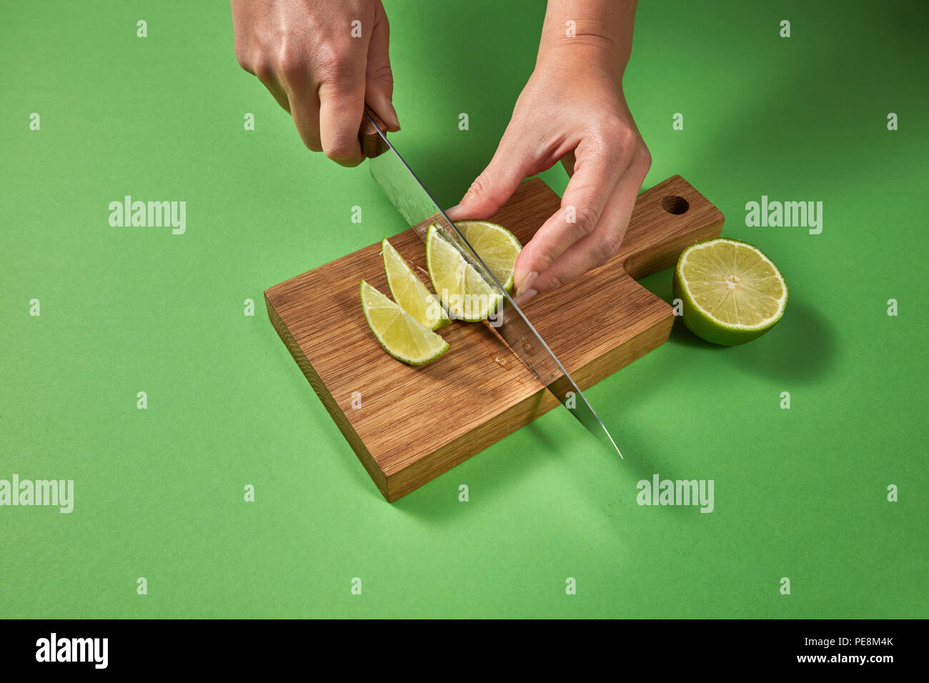 Tranches de citron vert biologique naturel, découpage, par des mains sur une planche en bois sur fond vert avec copie espace. Banque D'Images