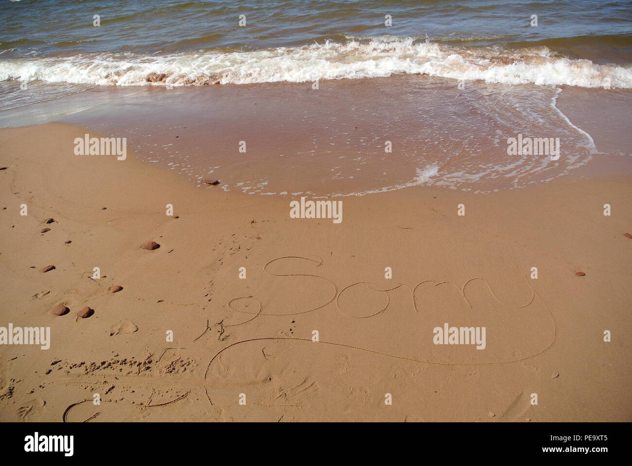 Un beau message appology 'Désolé' dans un style manuscrite cursive sur le sable rouge sur une plage avec une vague venant dans la partie supérieure, PEI, Canada Banque D'Images