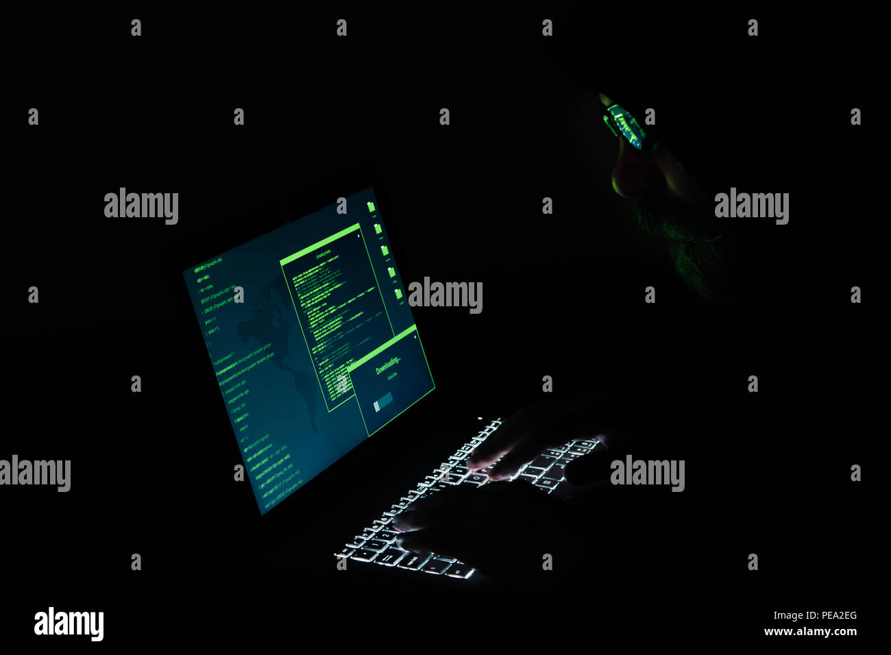Hacker à capuchon dans une pièce sombre l'exécution d'une cyber-attaque. Ordinateur portable écran et clavier éclairé. Banque D'Images