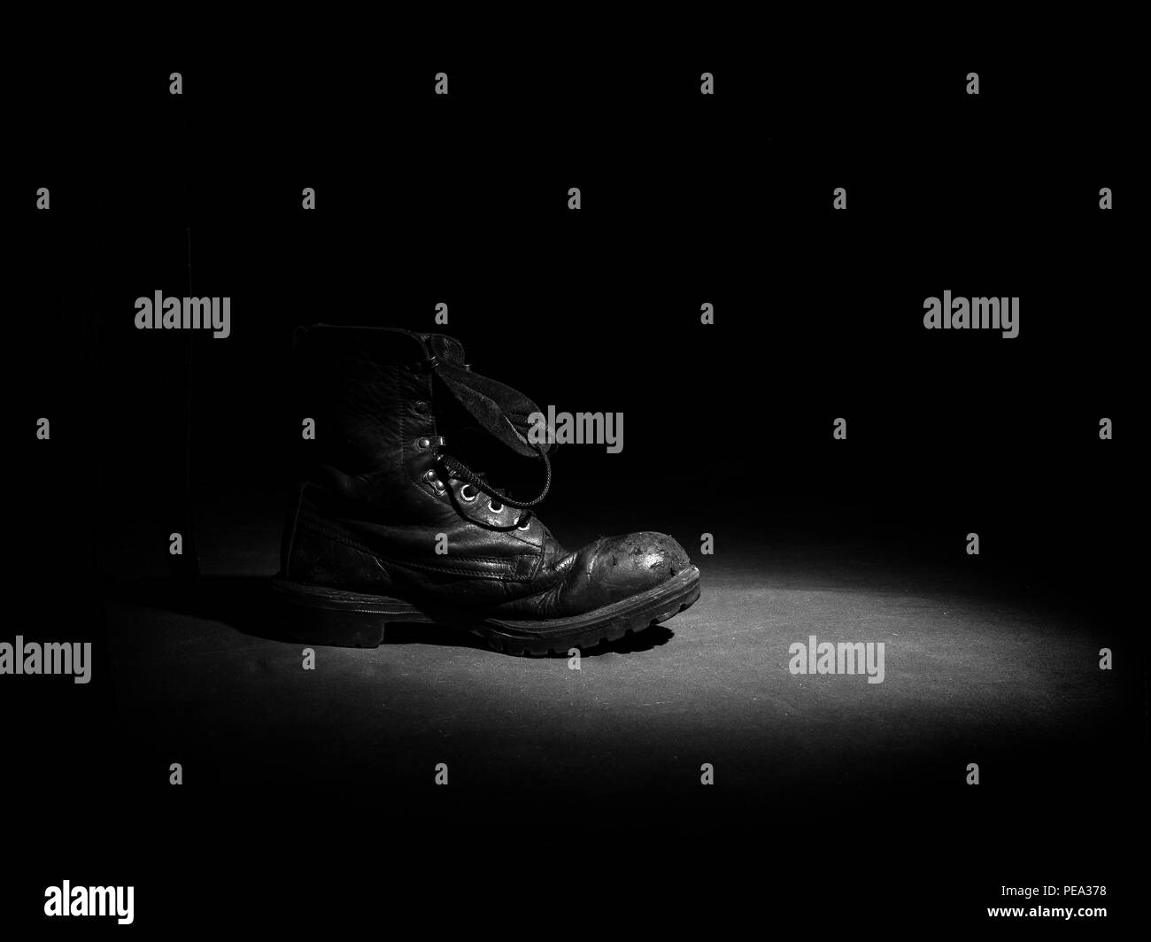 Ancienne chaussure militaire dans un rayon de lumière en noir et blanc. Banque D'Images