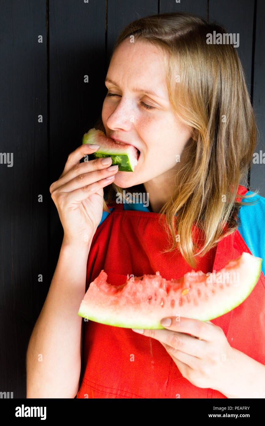 Une belle et jeune fille mord un frais, délicieux et juteux melon d'eau. Il est très faim et veut manger. La pastèque, elle a éclaté en deux petites Banque D'Images