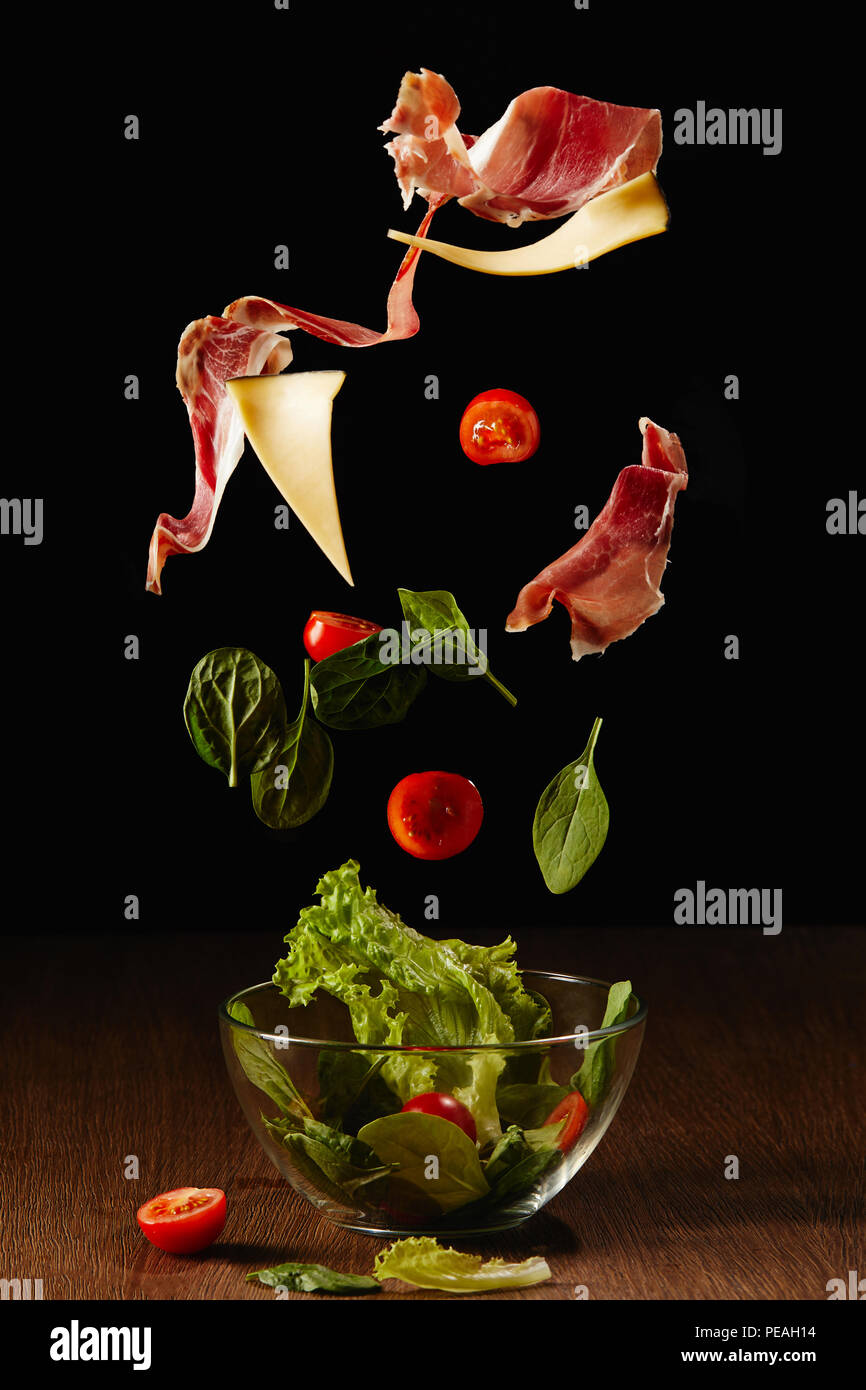 Ingrédients pour salade de légumes et de jambon dans un bol de tomber au-dessus de table en bois Banque D'Images