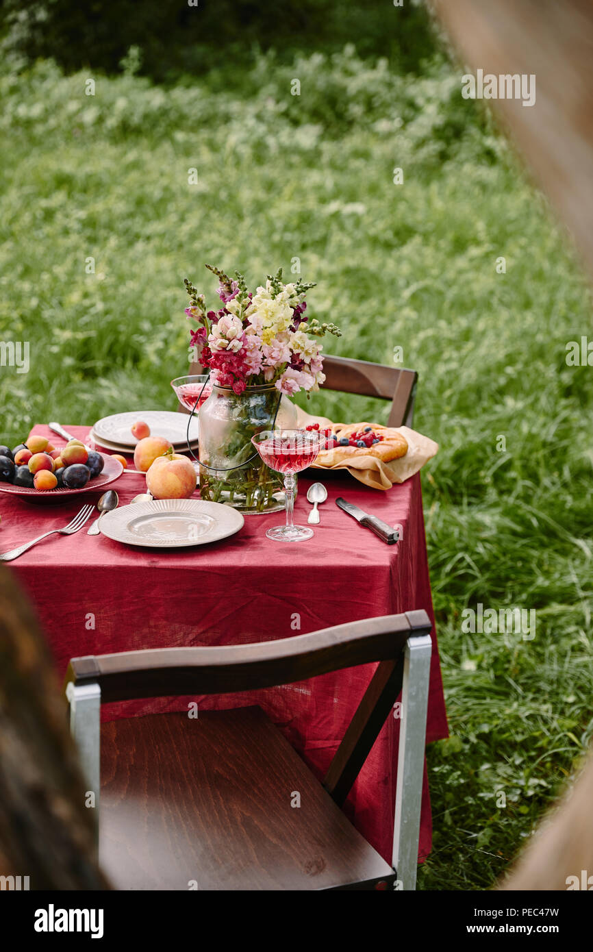 Bouquet de fleurs dans un bocal en verre et des fruits sur la table de jardin Banque D'Images