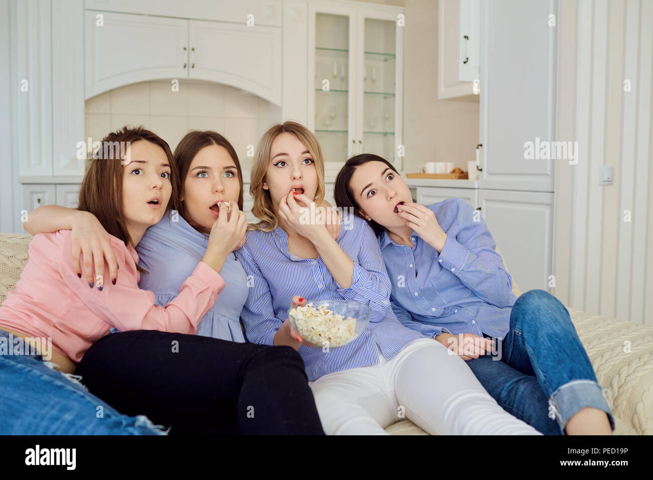 Les jeunes filles de regarder la télévision, eating popcorn assis sur le canapé. Banque D'Images