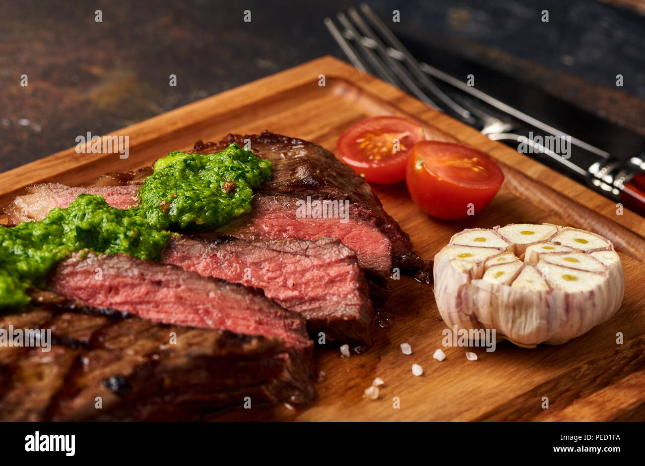 Black Angus Steak grillé avec Tomates, ail avec sauce Chimichurri la viande sur une planche à découper. Banque D'Images