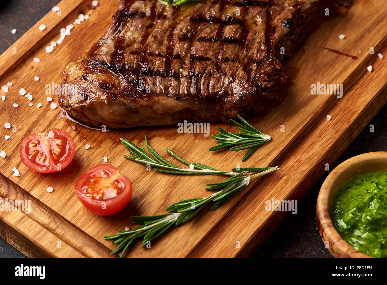 Black Angus Steak grillé avec Tomates, ail avec sauce Chimichurri la viande sur une planche à découper. Banque D'Images