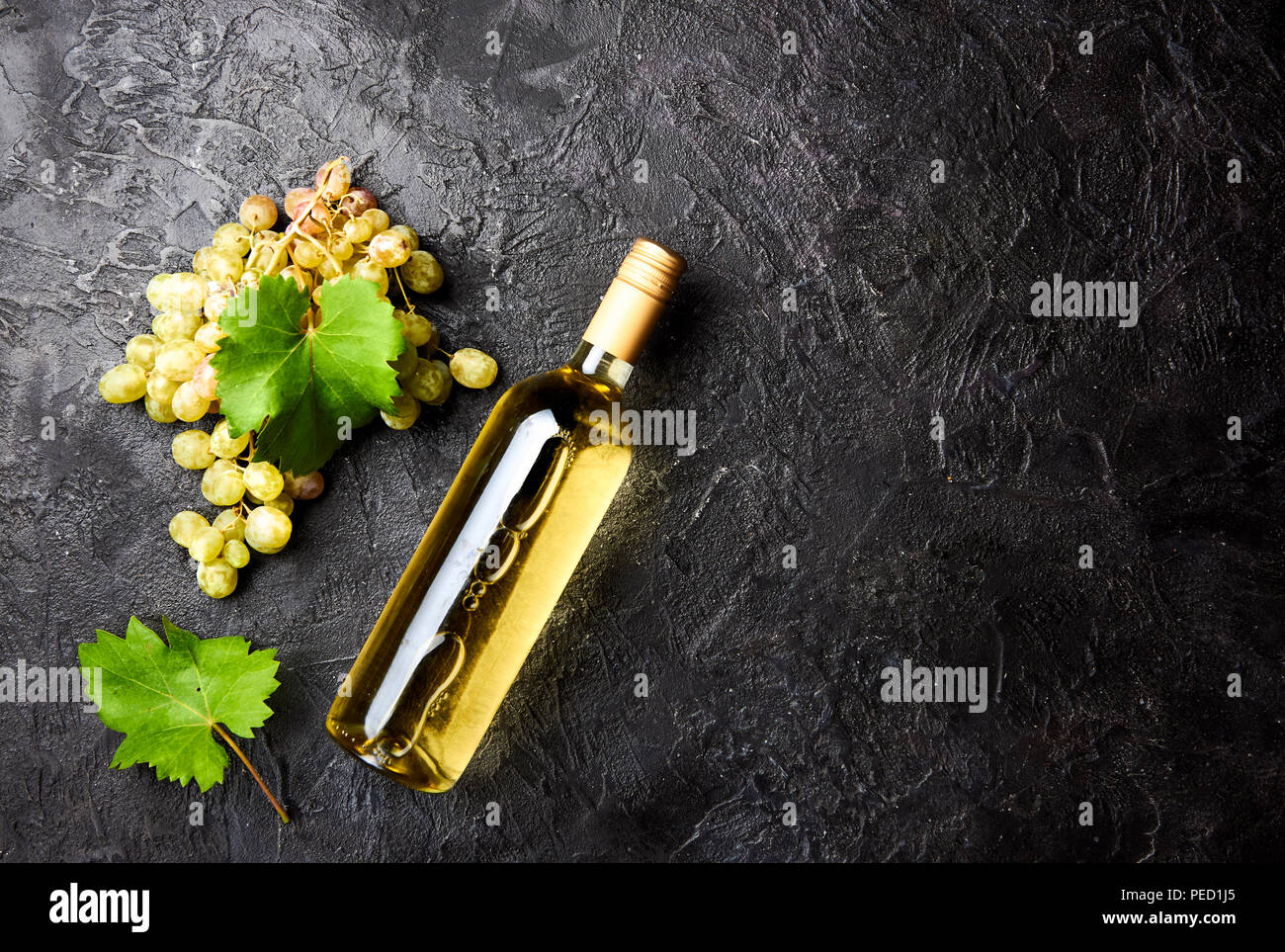 Bouteille de vin blanc avec des raisins et des feuilles de vigne sur fond de béton foncé. Banque D'Images