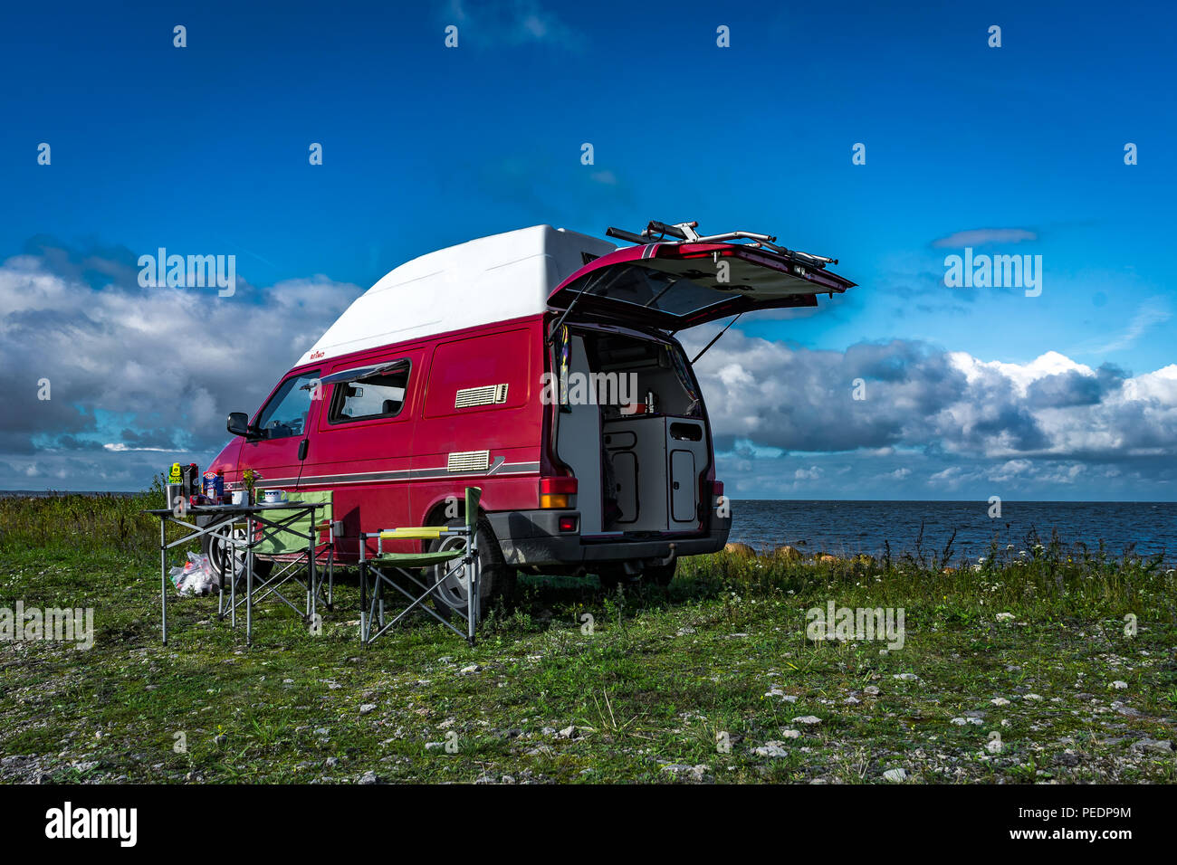 Estonie - Août 2018 : VW Transporter T4 sur mer baltique avec coucher du soleil en arrière-plan et ciel bleu avec des nuages. Au premier plan, l'équipement de camping est situé Banque D'Images