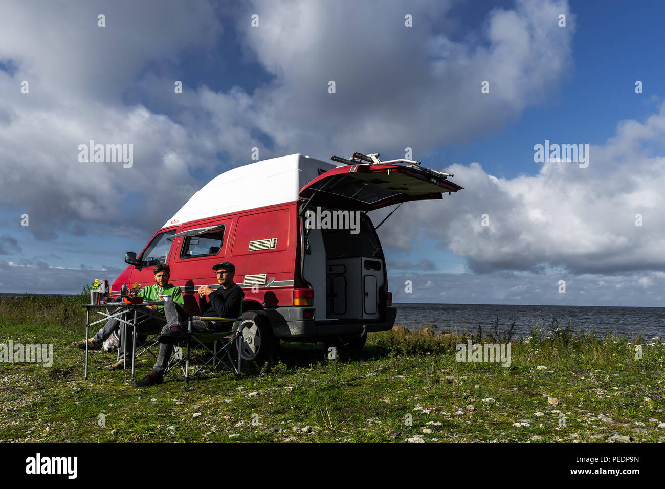 Estonie - Août 2018 : VW Transporter T4 sur mer baltique avec coucher du soleil en arrière-plan et ciel bleu avec des nuages. Au premier plan, l'équipement de camping est situé Banque D'Images