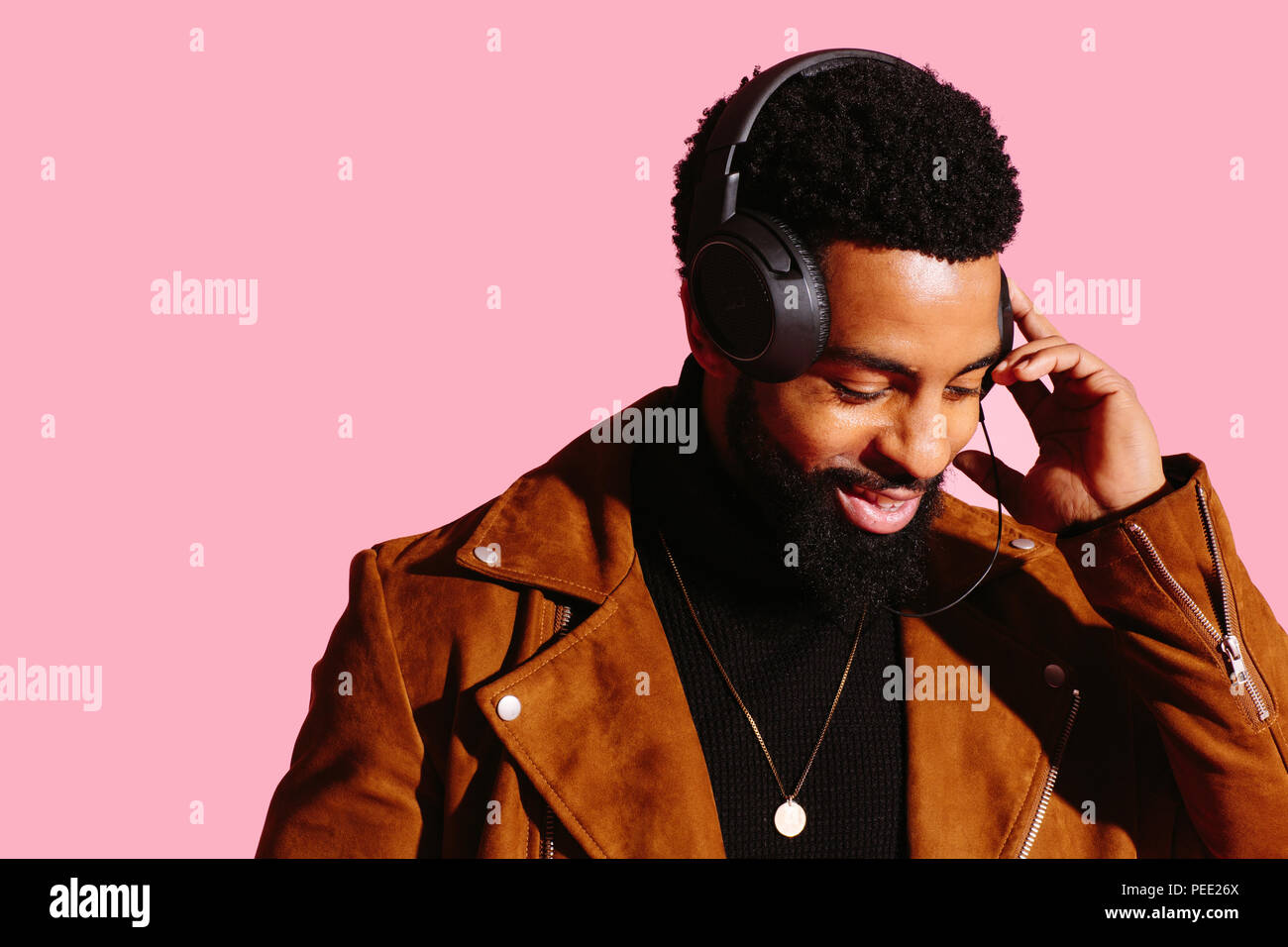 Portrait of a smiling man with beard et écouteurs, à écouter de la musique vers le bas, isolé sur fond de studio rose Banque D'Images