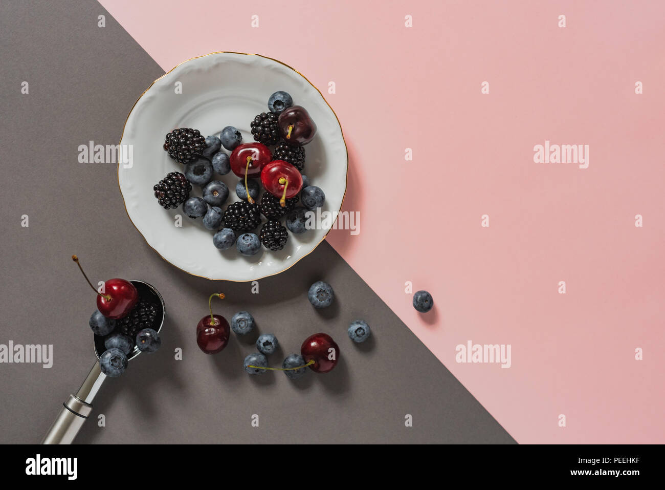 Flatlay de baies sur plaque blanche et crème glacée cuillère sur fond gris et rose. Banque D'Images