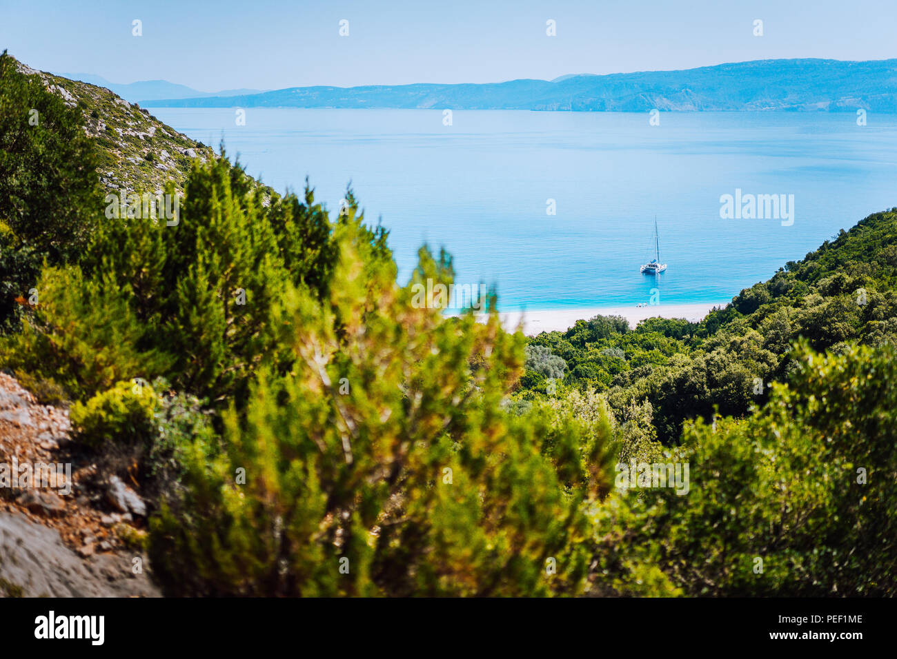 Yacht à Fteri solitaire masqué plage lagon, Kefalonia, Grèce. Vue encadrée entre les branches d'arbre de pin pendant le trekking vers le bas chemin ravin Banque D'Images