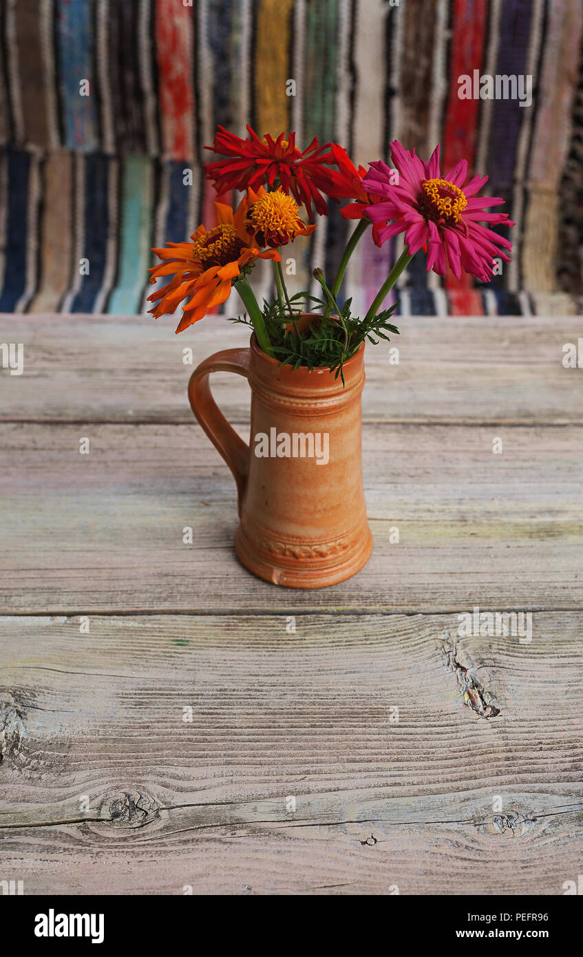 Des fleurs colorées dans la vieille tasse en céramique sur la vieille table en bois, tapis colorés en arrière-plan. Banque D'Images