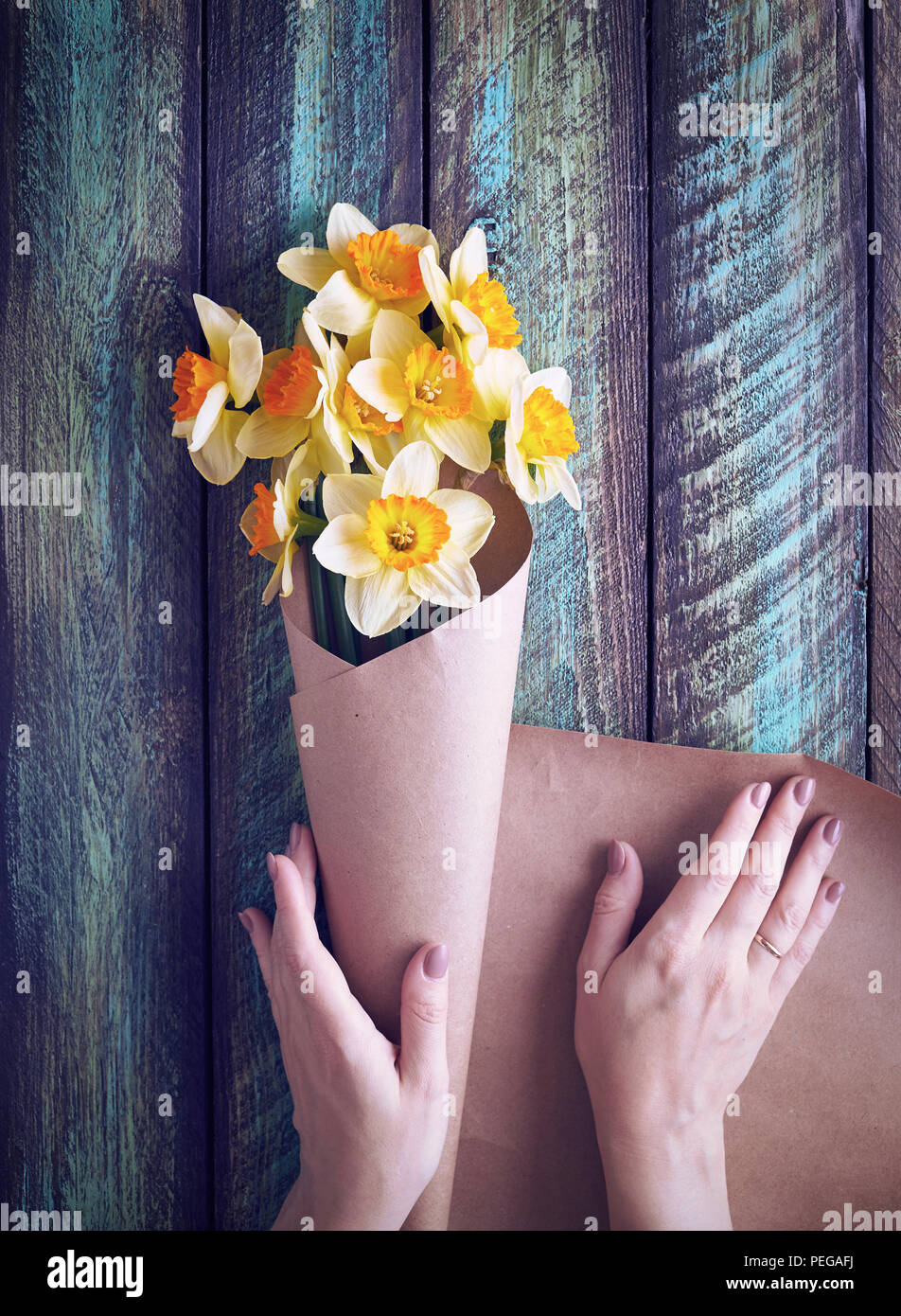 Woman wrapping narcisse bouquet dans du papier brun vert sur fond de bois Banque D'Images