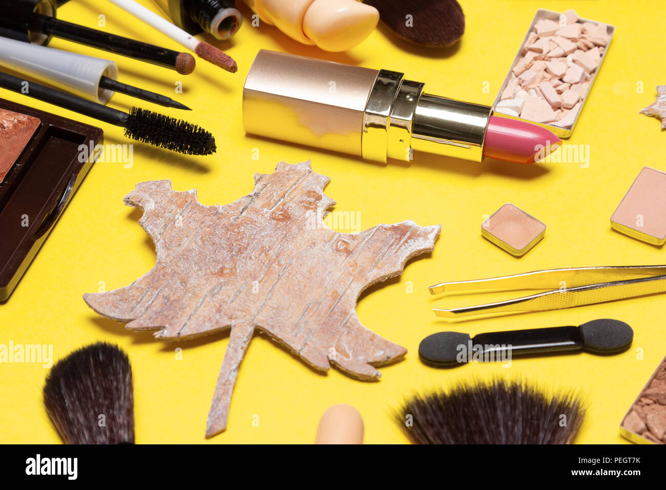 Maquillage d'automne. Produits et accessoires de maquillage avec maple leaf fait d'écorce sur fond jaune. Close up, selective focus Banque D'Images
