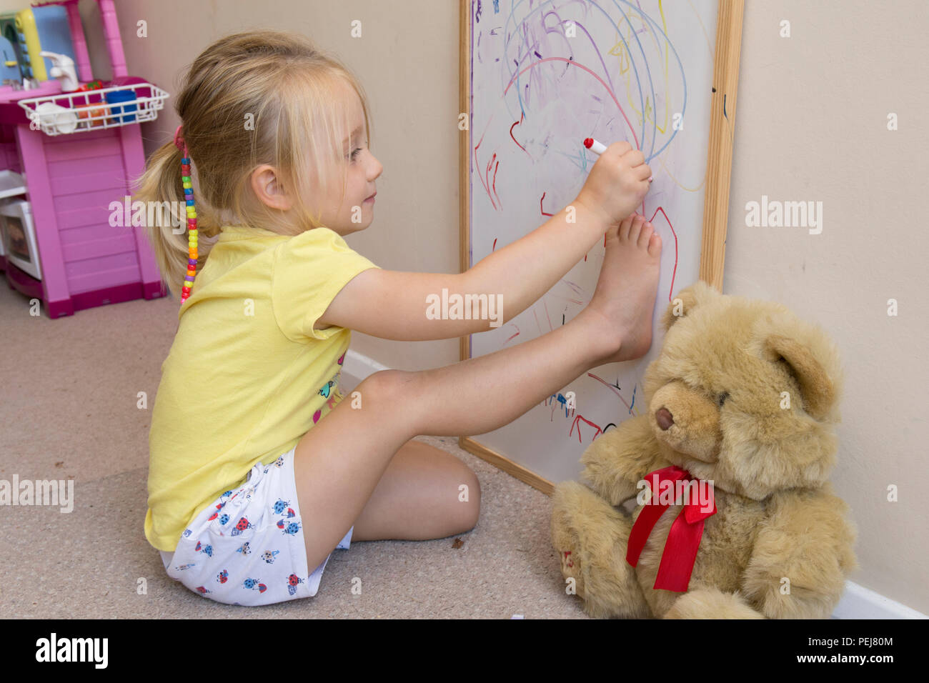 Jeune fillette de deux ans le dessin avec un stylo de couleur sur un tableau blanc en cours de dessin artistique, autour de l'esquisse de son pied. Banque D'Images