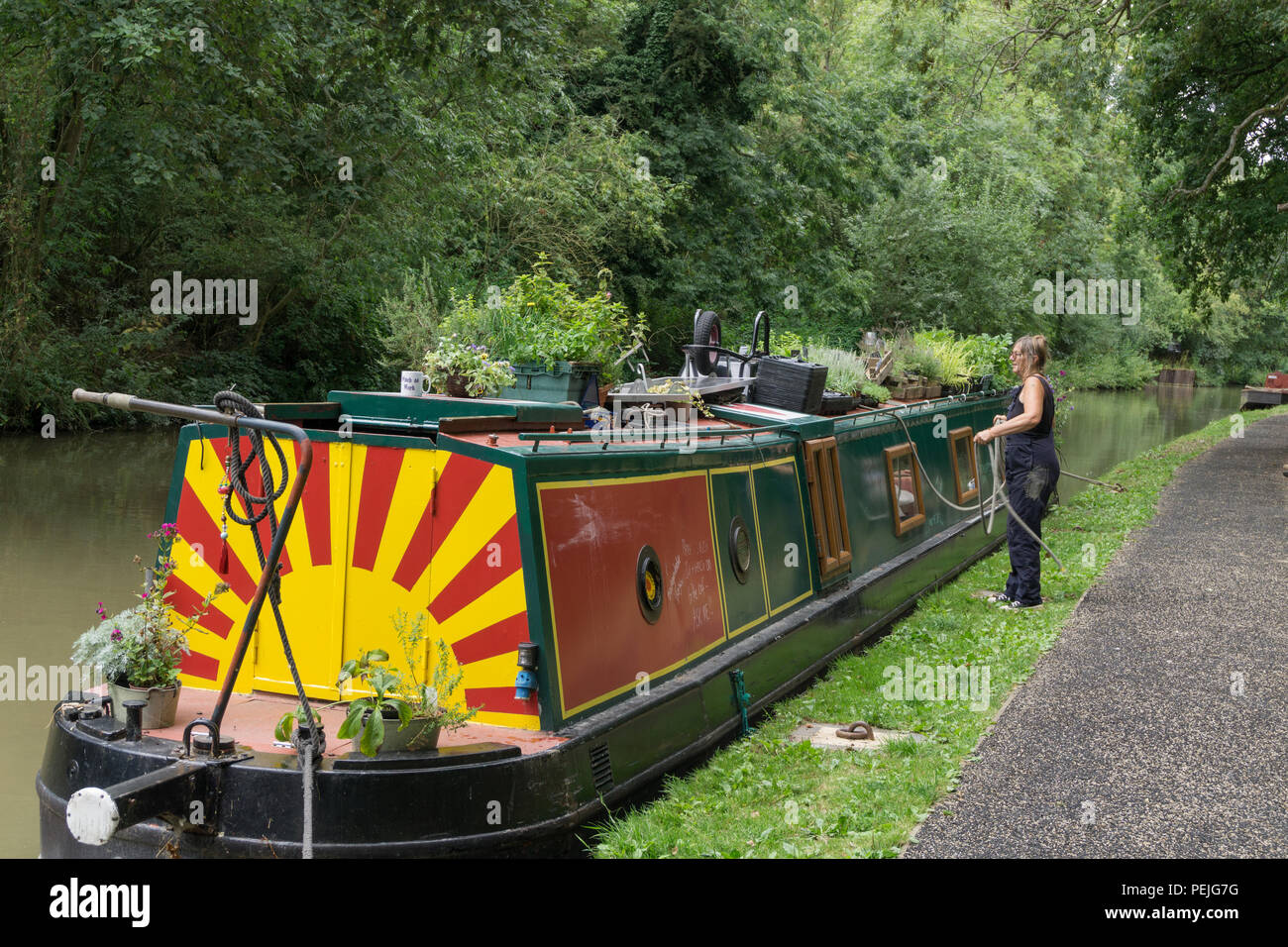 Femme l'amarrage d'un grand classique sur le canal, à Stoke Bruerne, Northamptonshire, Royaume-Uni ; l'arrière du bateau décoré avec le soleil levant. Banque D'Images