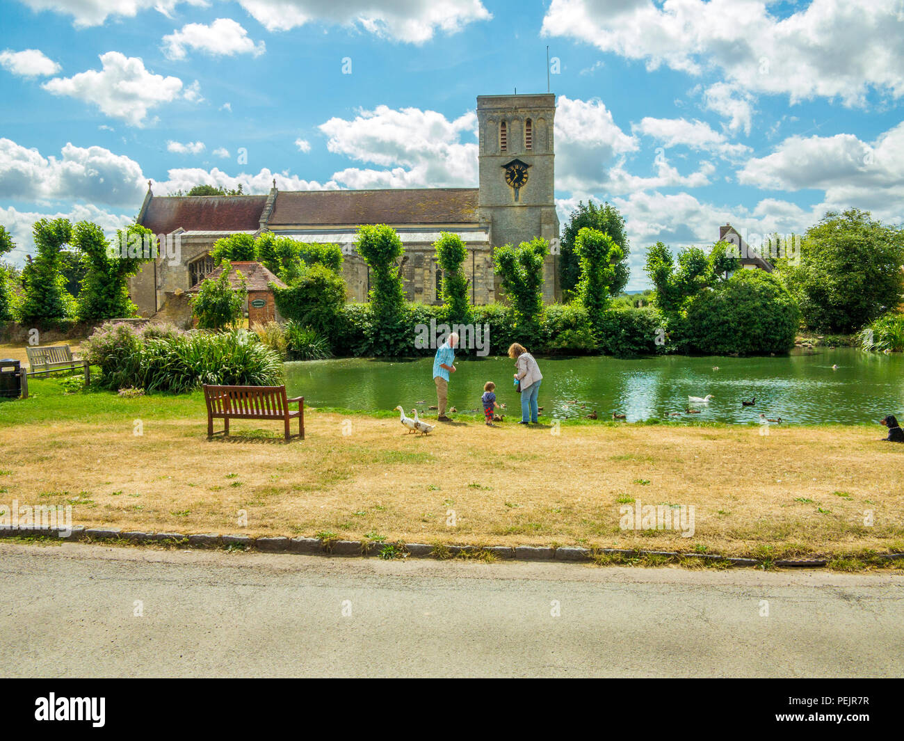 La quintessence du village anglais vert avec l'alimentation de la famille canards sur l'étang et l'église de St Mary the Virgin à Haddenham Buckinghamshire Angleterre Banque D'Images