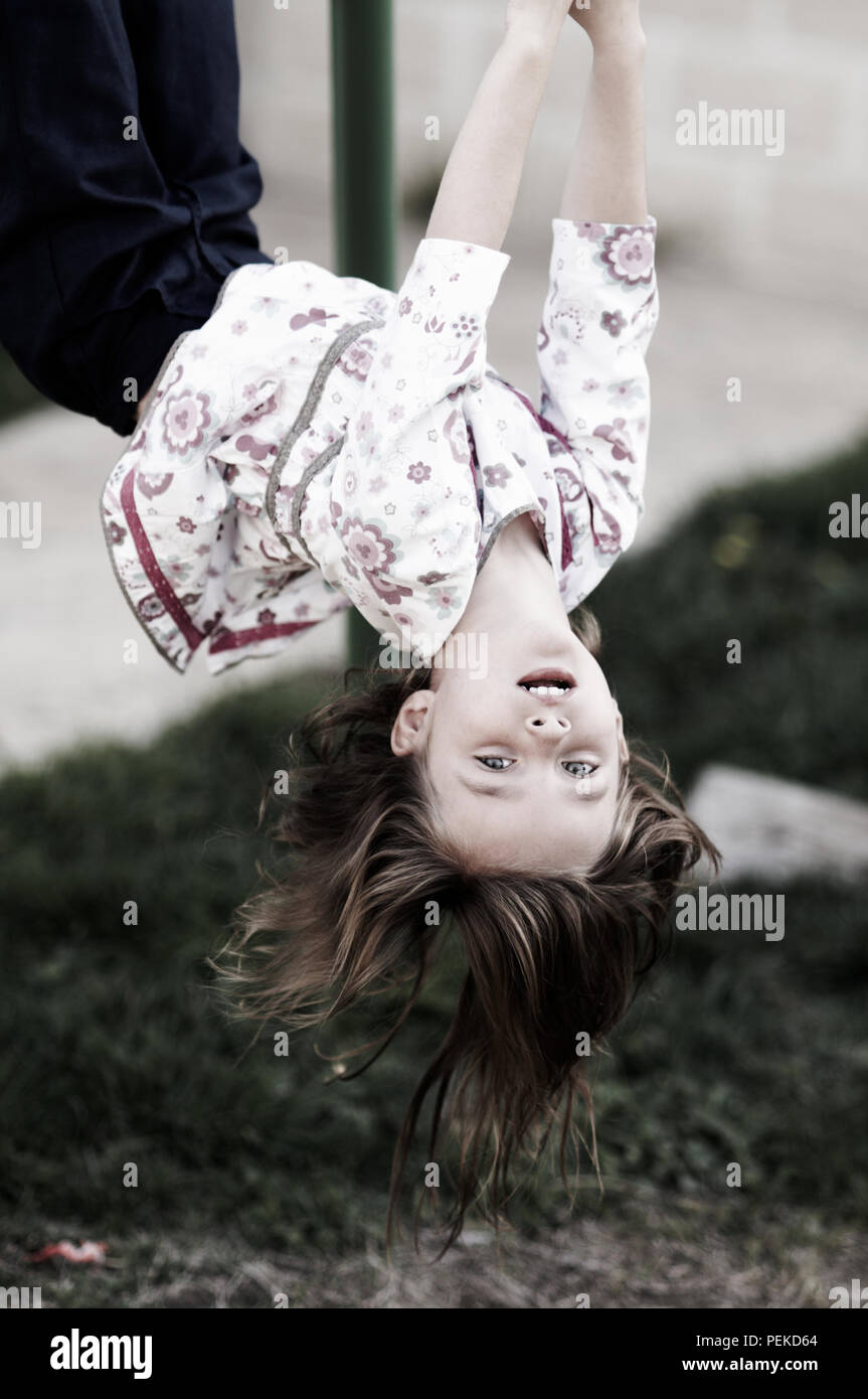 Petite fille innocente à jouer tête en bas sur les barres. Banque D'Images