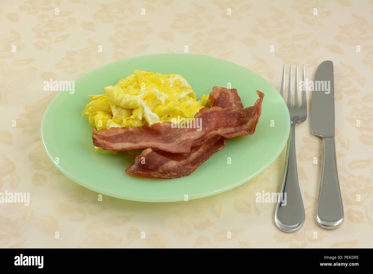 Rapide petit déjeuner d'œufs brouillés et de 2 bandes de bacon de dinde sur plaque verte avec fourchette et couteau Banque D'Images