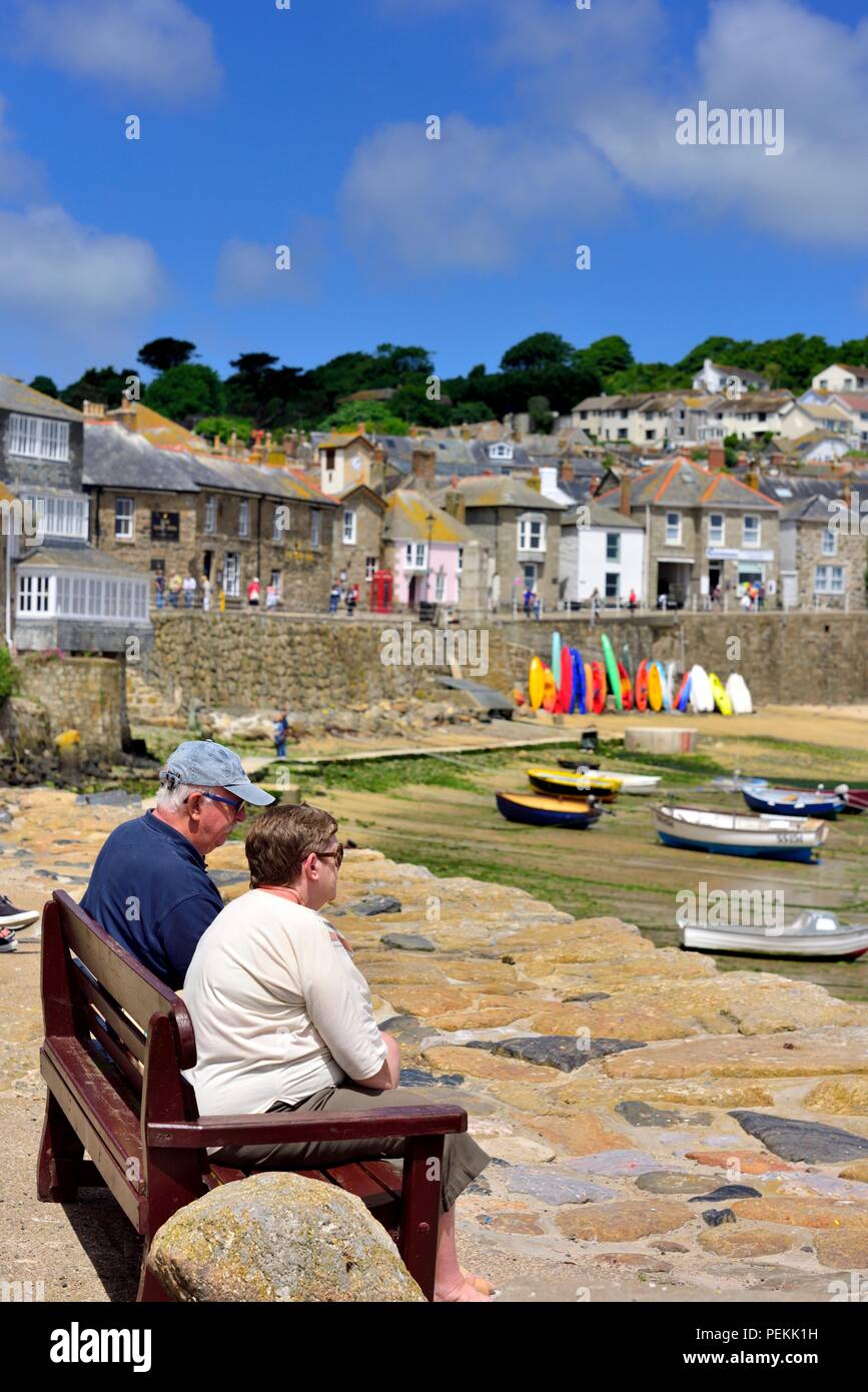 2 deux personnes assises sur des bancs dans le soleil d'été dans le village de pêcheurs de Mousehole, Cornwall, Angleterre, Royaume-Uni Banque D'Images