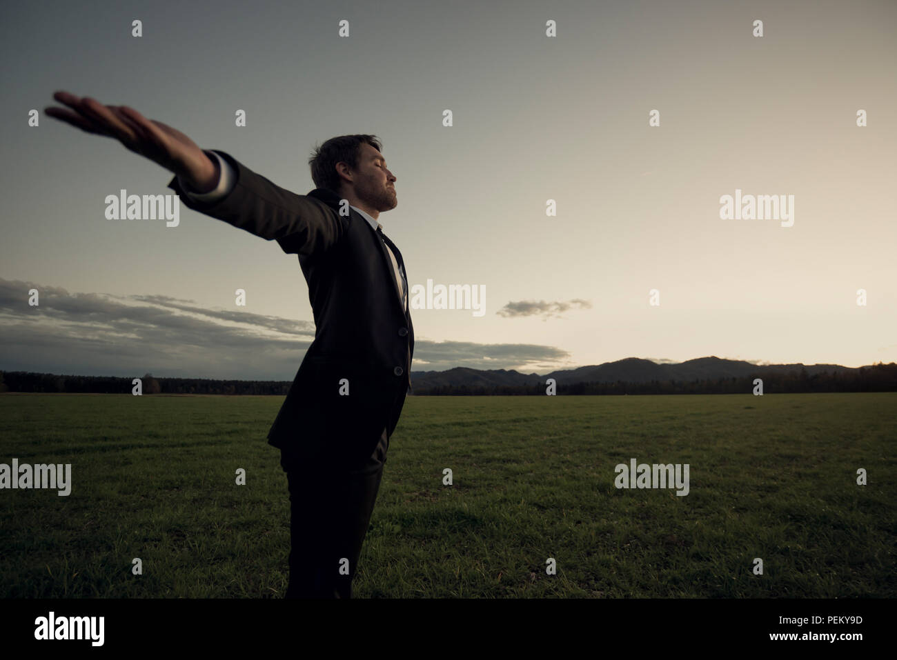 Vue latérale d'un jeune homme debout au champ avec large bras ouverts. Banque D'Images