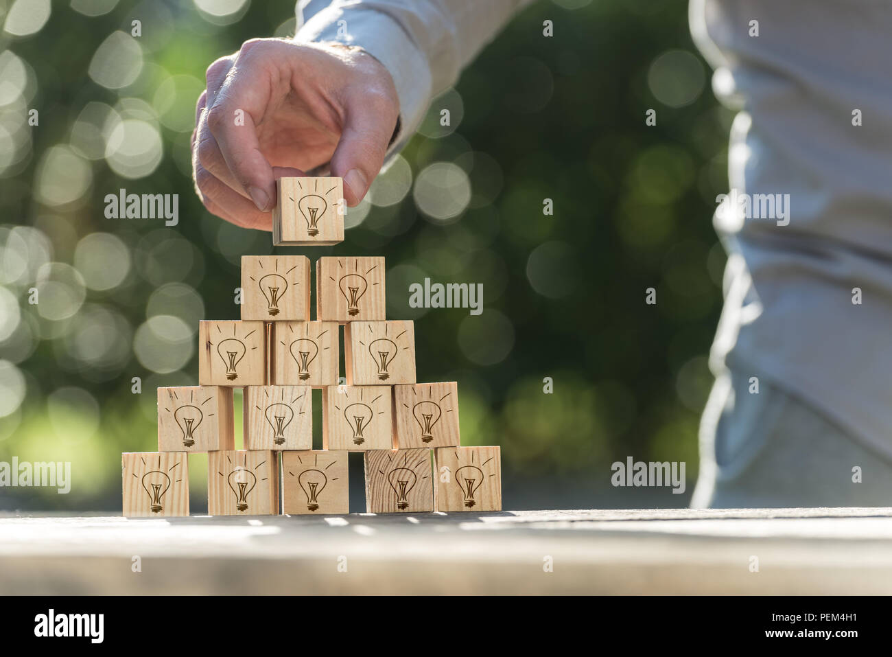 Une vision et des idées concept d'un homme la construction d'une pyramide de blocs en bois avec des icônes sur l'ampoule contre bokeh mousseux. Banque D'Images