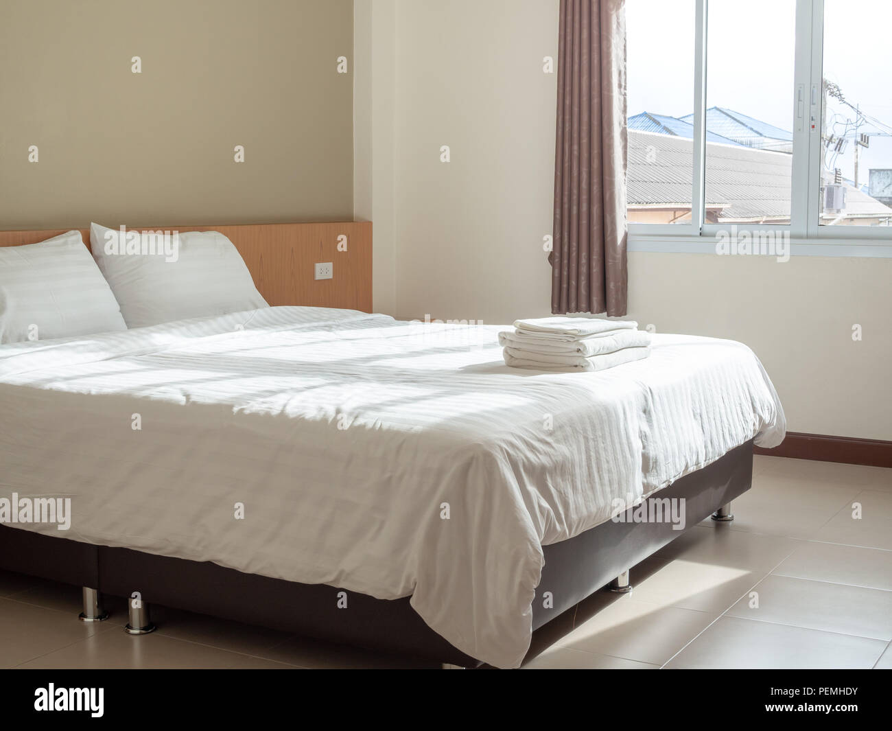 Chambre propre blanc dans l'hôtel, oreillers et serviettes sur le lit, les rideaux et la lumière de la fenêtre de l'extérieur avec vue sur la campagne environnante. dans les maisons Banque D'Images