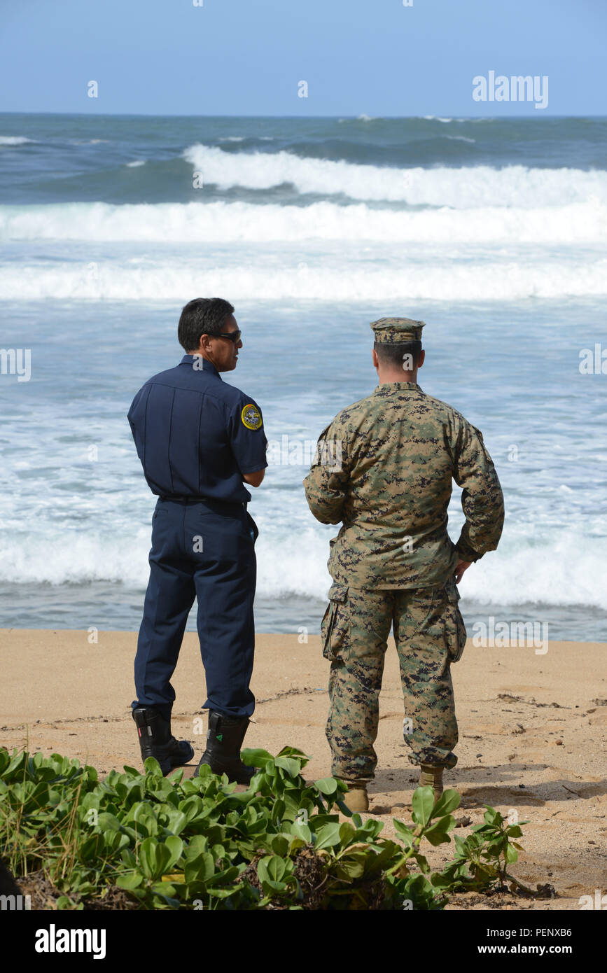 Membres de l'équipage du Marine Corps et Honolulu pompiers ont une discussion sur la plage, à l'Haleiwa Beach Park poste de commandement au cours de la recherche, de 12 aviateurs marins au large de la côte nord d'Oahu, 16 janvier 2016. La Garde côtière canadienne et plusieurs organismes partenaires sont la poursuite de la recherche après l'avis de deux hélicoptères militaires abattus, chacun aurait été avec six membres du personnel à bord, 14 janvier 2016. (U.S. Photo de la Garde côtière du Maître de 2e classe Tara Molle/libérés) Banque D'Images