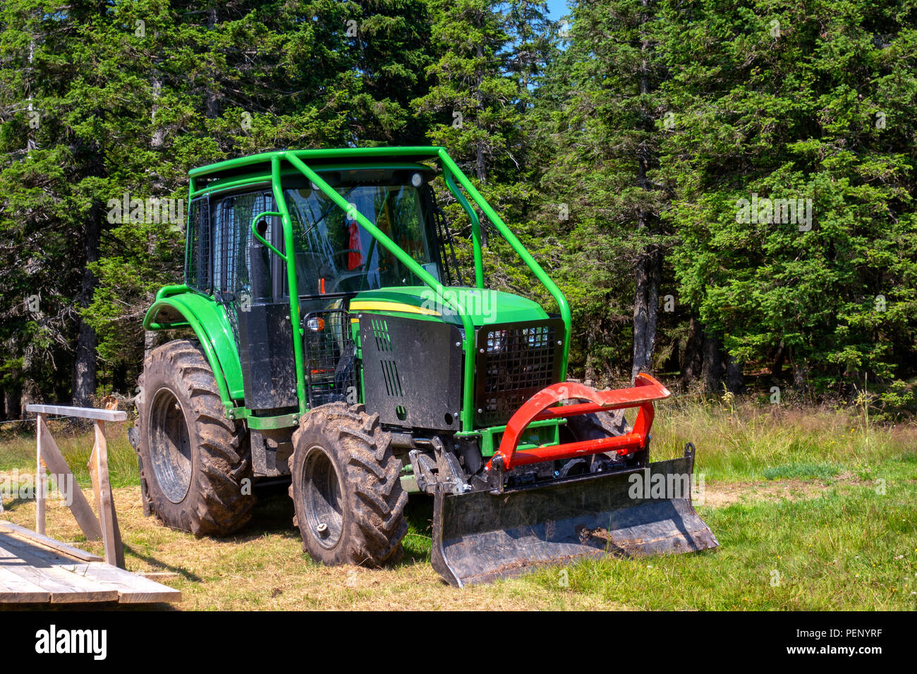 Tracteur forestier vert avec rouleau cage et charrue, machines pour l'industrie du bois, bois en arrière-plan Banque D'Images