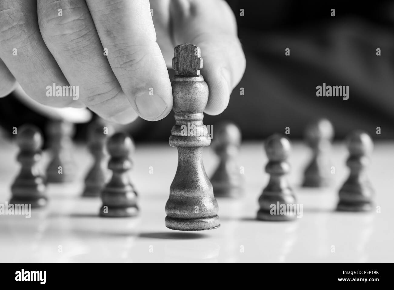 Businessman jouant aux échecs en déplaçant le roi morceau soulevant dans ses doigts en noir et blanc. Banque D'Images