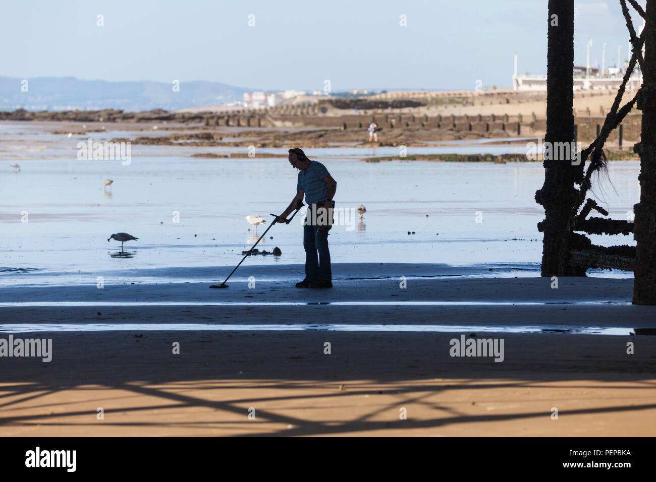 Hastings, East Sussex, UK. Août 17, 2018. UK : météo chaude et ensoleillée matin à Hastings, East Sussex avec beaucoup de gens sur la plage. Les températures devraient dépasser les 21°C. Un detectorist arpente la plage à la recherche de trésor perdu avec un détecteur de métal alors que la marée est sous la jetée. © Paul Lawrenson, 2018 Crédit photo : Paul Lawrenson / Alamy Live News Banque D'Images