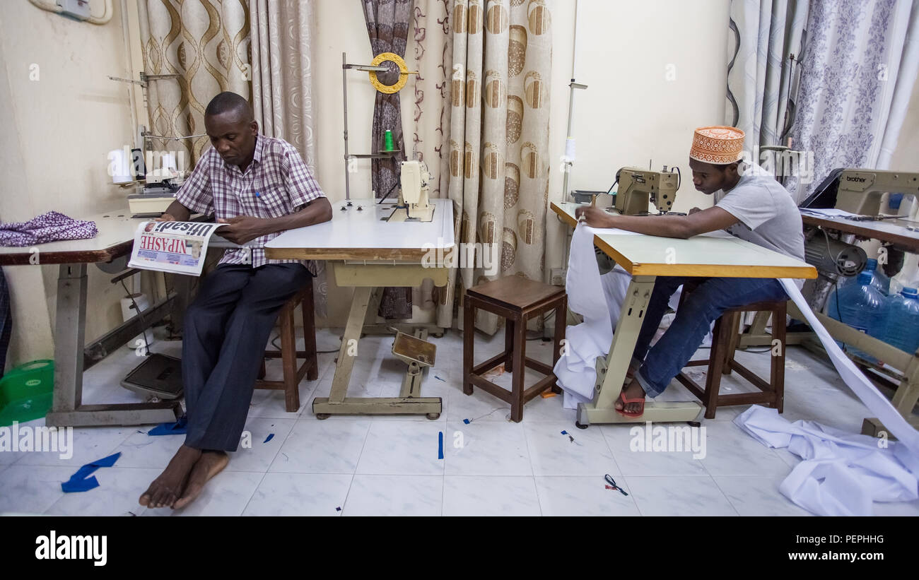 Stone Town, Zanzibar, 13 Janvier - 2015 : atelier de couture avec jeune homme l'ensemencement et vieil homme lecture. Banque D'Images