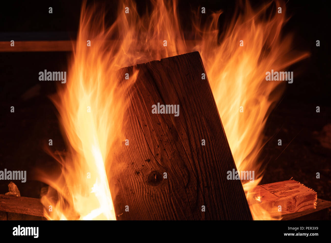 Un feu de bois blazes dans un foyer comme des membres de la famille et amis se rassemblent autour de la nuit pour rôtir des guimauves Banque D'Images