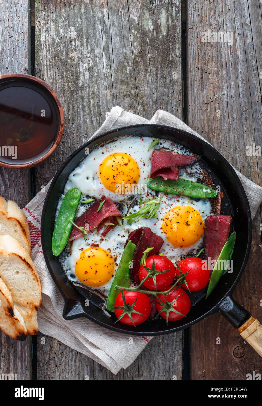 Oeufs frits dans une poêle avec les tomates cerises, les pois verts et le pastrami. Copyspace Banque D'Images