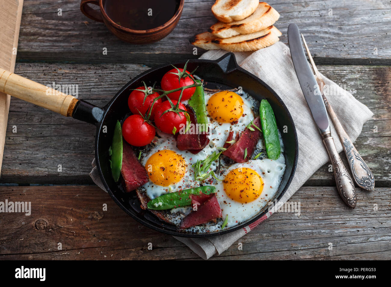 Oeufs frits dans une poêle avec les tomates cerises, les pois verts et le pastrami. Copyspace Banque D'Images