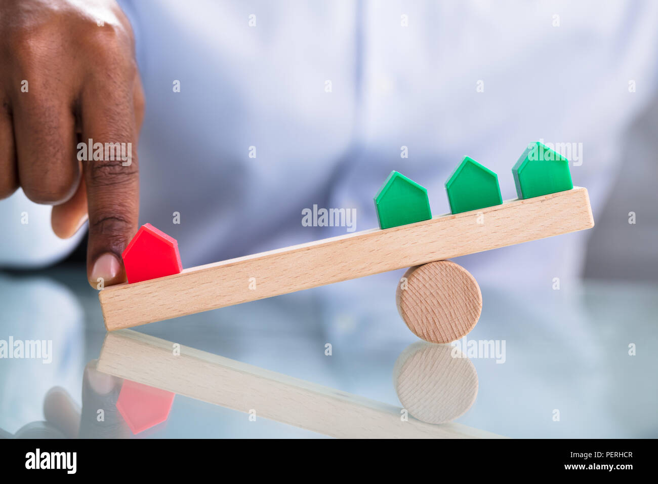 La main de l'équilibre entre rouge et vert maison miniature en bois au cours de la balançoire sur bureau réfléchissant Banque D'Images