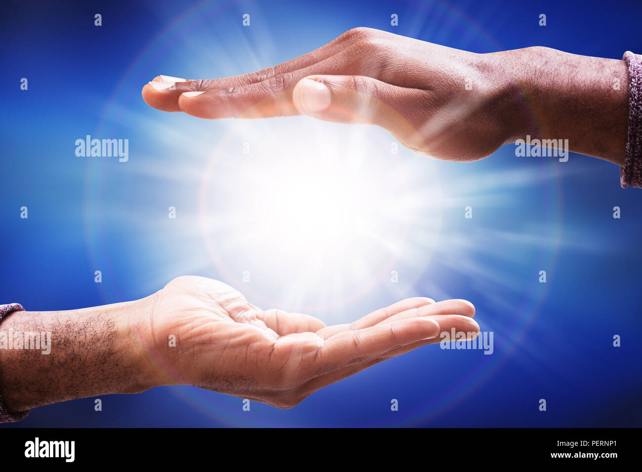 La main du mâle la collecte de la lumière du soleil rougeoyant Flare contre fond bleu Banque D'Images