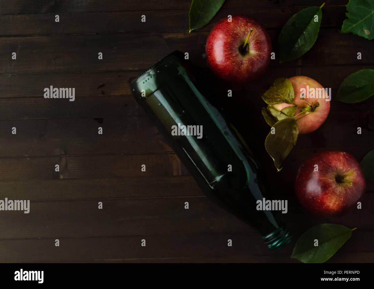 Une bouteille de vinaigre de cidre avec trois pommes fraîches et de feuilles vertes sur fond de bois..Copyspace gauche. Banque D'Images